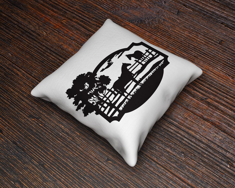 May include: White square throw pillow with a black silhouette design of a horse, fence, tree, and landscape. The pillow is on a dark wood surface.