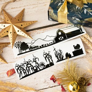 Op de afbeelding: Drie zwart-witte silhouet stickers met een boerderij met een schuur, ma&iuml;sstengels en een kalkoen. De stickers zijn op een witte achtergrond met een houten oppervlak en gouden stervormige ornamenten.