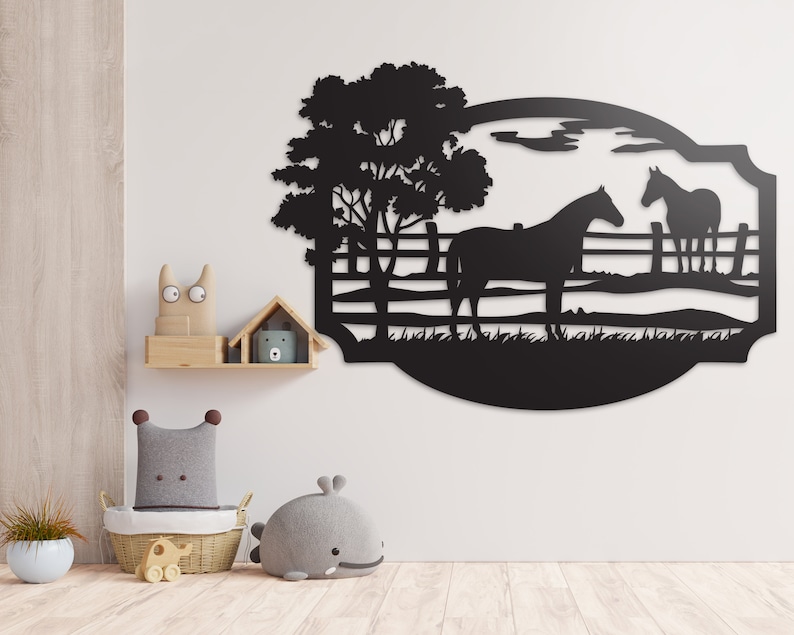 May include: Black metal wall art featuring two horses in a pasture with a tree and fence. The artwork is cut in a silhouette style, with a curved border. The background is a light-colored wall.