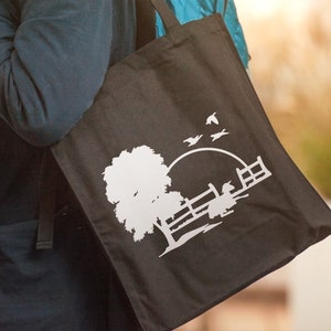 Peut inclure: Un sac fourre-tout noir avec un motif en silhouette blanche d'un arbre, une cl&ocirc;ture et des oiseaux volant au-dessus d'un soleil couchant.
