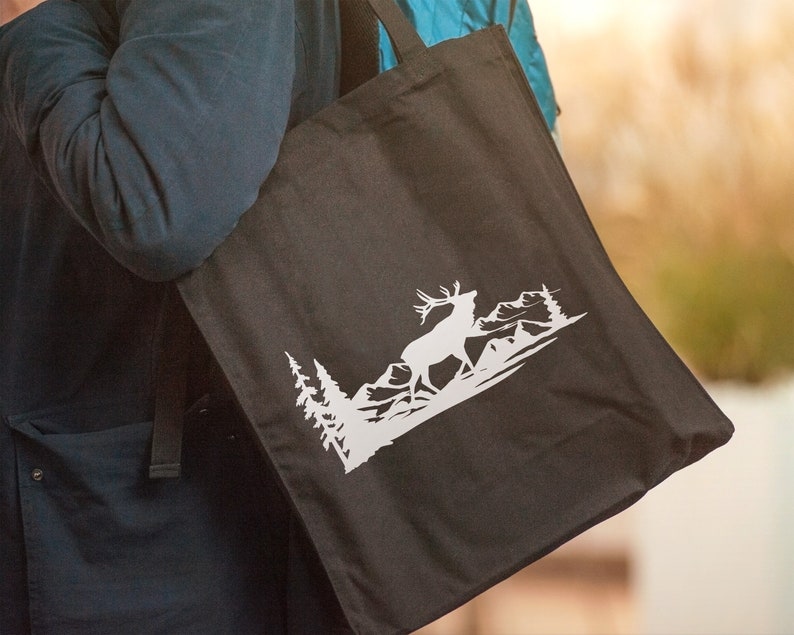 May include: A black tote bag with a white silhouette of an elk standing in a mountain landscape. The elk is facing right and has large antlers.