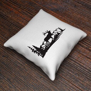 May include: A white throw pillow with a black silhouette of a deer walking through a forest. The deer is in the foreground and the trees are in the background.
