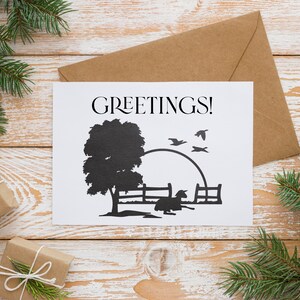 Peut inclure: Une carte blanche avec le mot "GREETINGS!" imprim&eacute; en noir. La carte pr&eacute;sente une silhouette noire d'un arbre, d'une cl&ocirc;ture, d'un oiseau et d'un petit animal. La carte est pos&eacute;e sur une surface en bois avec une enveloppe brune derri&egrave;re elle.