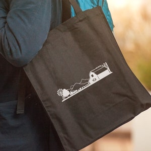 Op de afbeelding: Een zwarte tote bag met een wit silhouet van een boerderij en een windmolen.