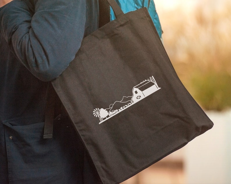 Op de afbeelding: Een zwarte tote bag met een wit silhouet van een boerderij en een windmolen.