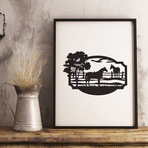 May include: Black framed art print featuring a silhouette of two horses in a pasture with a tree. The artwork is set against a white background, with a black border. The print is displayed on a wooden surface.