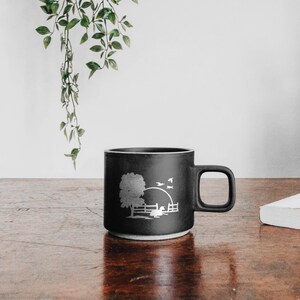 Peut inclure: Une tasse en c&eacute;ramique noire avec un motif en silhouette blanche d'un arbre, d'une cl&ocirc;ture et d'oiseaux sur fond de coucher de soleil.