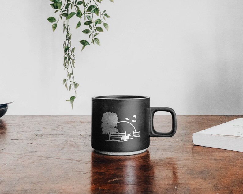 Peut inclure: Une tasse en c&eacute;ramique noire avec un motif en silhouette blanche d'un arbre, d'une cl&ocirc;ture et d'oiseaux sur fond de coucher de soleil.