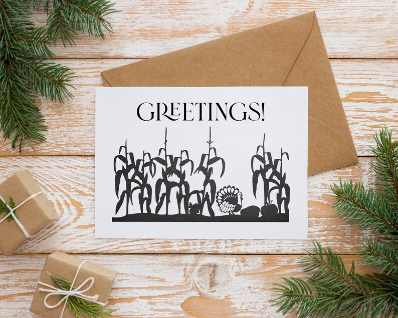 Op de afbeelding: Een witte kaart met de tekst "GREETINGS!" in het zwart gedrukt. De kaart toont een zwart silhouet van een kalkoen die in een ma&iuml;sveld staat.