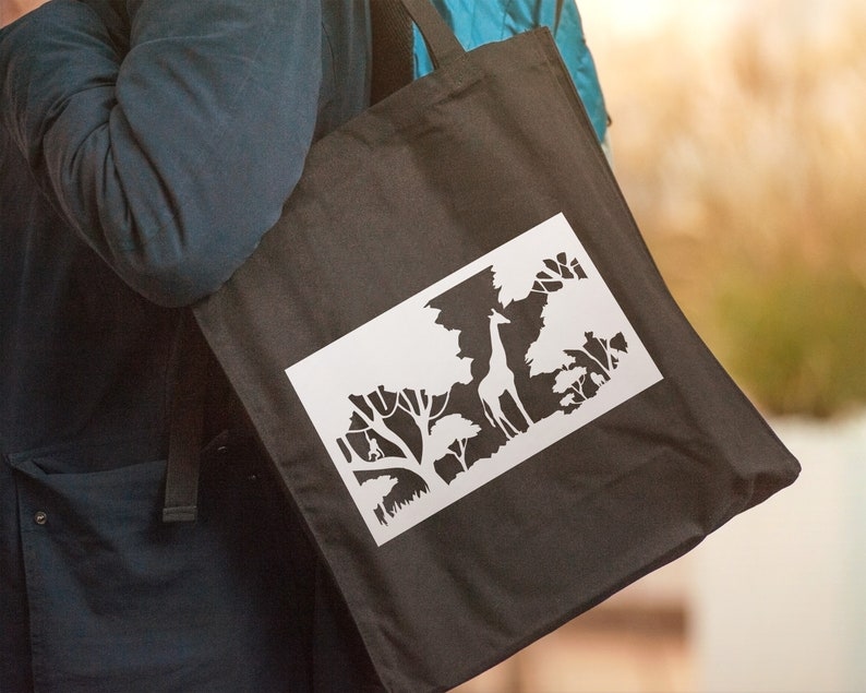 May include: A black tote bag featuring a white silhouette of a giraffe in a forest scene.