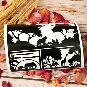 May include: Black and white stencil sheet featuring four different designs. The designs include a lion, a giraffe, an elephant, and a sunset scene. The stencil sheet is ideal for crafting and DIY projects.