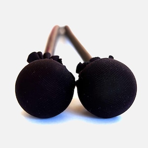 May include: A pair of black marimba mallets. Each mallet features a spherical head with a textured surface, attached to a gray handle. The heads are made of a dark fabric, and the handles are connected by a curved metal piece.