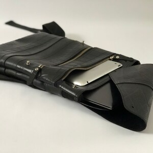 May include: Black messenger bag made from recycled tire material. The bag features a zippered main compartment, a front pocket, and a shoulder strap. A tablet and laptop are visible inside the bag.