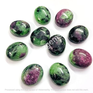 May include: A collection of oval-shaped ruby zoisite gemstones. The stones display a mix of green and dark pink hues, with a polished, glossy finish. The gemstones are arranged on a white surface.
