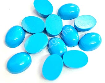 May include: A collection of polished, oval-shaped turquoise gemstones. The stones are a vibrant, solid blue colour and appear smooth and glossy. The gemstones are scattered across a white surface.