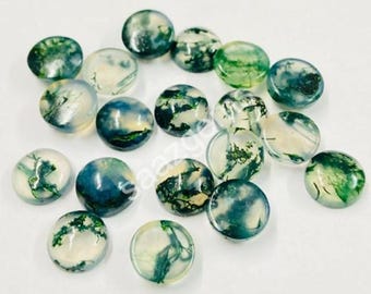 May include: A collection of round, polished gemstones with a mix of green, white, and blue hues. The stones have a translucent quality, with patterns resembling landscapes. The gemstones are scattered on a white surface.