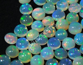 May include: A collection of round, polished opal gemstones. The opals display a range of colors, including blue, green, and flashes of orange and yellow. The gemstones are set against a black background.