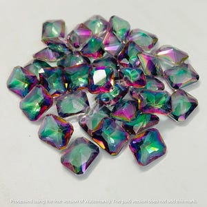 May include: A collection of iridescent, square-cut rhinestones. The gems display a spectrum of colors, including green, purple, and pink, with a reflective, multi-faceted surface. The rhinestones are scattered on a white background.