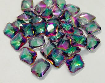 May include: A collection of iridescent, square-cut rhinestones. The gems display a spectrum of colors, including green, purple, and pink, with a reflective, multi-faceted surface. The rhinestones are scattered on a white background.