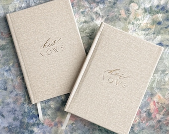 May include: Two rectangular hardcover books with a textured beige fabric cover. One book features the text "his VOWS" in elegant brown script and print, while the other features the text "her VOWS" in the same style. Each book has a white ribbon bookmark.
