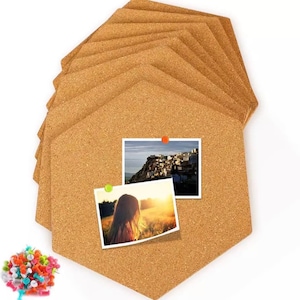 May include: A stack of hexagonal cork boards with two photos pinned to one board. The photos are held in place with orange and green push pins. A pile of colorful push pins is in the lower left corner. The cork boards are a light brown color.