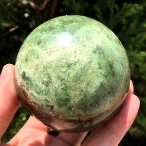 May include: A green and brown polished sphere of green opal, a type of gemstone.