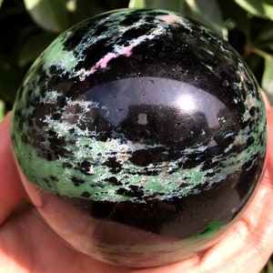 May include: A polished green and black sphere with swirling patterns. The sphere is made of a natural stone and has a smooth, glossy finish.