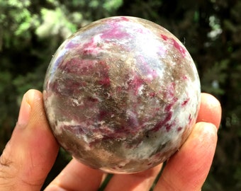 May include: A polished sphere of pink and gray gemstone with a swirling pattern. The sphere is smooth and reflective.