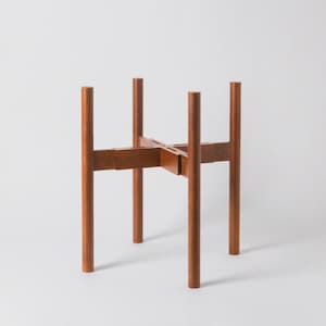 May include: A wooden plant stand with a mid-century modern design. The stand is made of brown wood and features four vertical legs connected by a cross-shaped support. The stand is designed to hold a potted plant. The stand is approximately 12 inches tall.