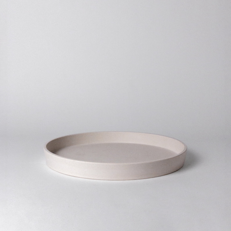 May include: A round, light beige ceramic tray with a slightly raised rim.