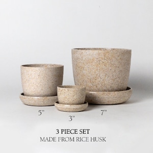 Op de afbeelding: Een set van drie beige bloempotten gemaakt van rijstzemelen. De potten hebben een diameter van 7,6 cm, 12,7 cm en 17,8 cm. De set is gelabeld "3 Piece Set Made From Rice Husk".