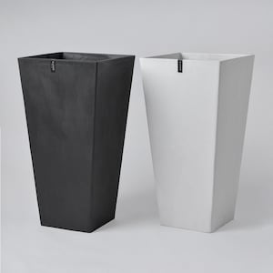 May include: Two tall, square-shaped planters. One is black, the other is white. Both have a tapered design, wider at the top and narrower at the base. Each planter has a small, rectangular label near the top. These planters are suitable for indoor or outdoor use.
