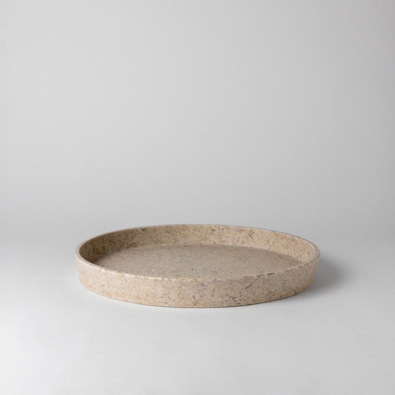 May include: A round, beige tray made of recycled materials. The tray has a rough, textured surface.