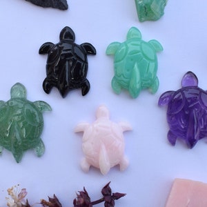 Könnte beinhalten: Fünf geschnitzte Schildkrötenfiguren aus verschiedenen Edelsteinen. Die Schildkröten sind grün, schwarz, rosa, lila und hellgrün.