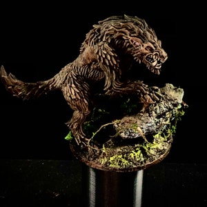 May include: A detailed, hand-painted miniature of a snarling, brown wolf with a mossy base. The wolf is sculpted with fur and sharp teeth, and its eyes are painted red.
