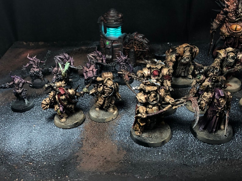 K&ouml;nnte beinhalten: Eine Sammlung von Miniaturfiguren, die in verschiedenen Braunt&ouml;nen, Gr&uuml;n- und Violettt&ouml;nen bemalt sind. Die Figuren sind auf einer grauen und braunen Oberfl&auml;che angeordnet. Einige der Figuren halten Waffen, w&auml;hrend andere in einer defensiven Haltung stehen.