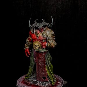 May include: A painted miniature figurine of a red-skinned humanoid warrior with large curved horns, wearing metallic shoulder armor and a gold belt featuring a skull emblem. The figure holds a large, flat, rectangular sword with ornate engravings.