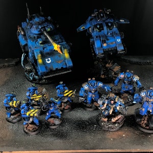 K&ouml;nnte beinhalten: Ein blaues und gelbes bemaltes Miniatur-Krieger-Armeeset mit zwei Fahrzeugen, einem Panzer und einem Flugobjekt sowie einer Soldatenstaffel.