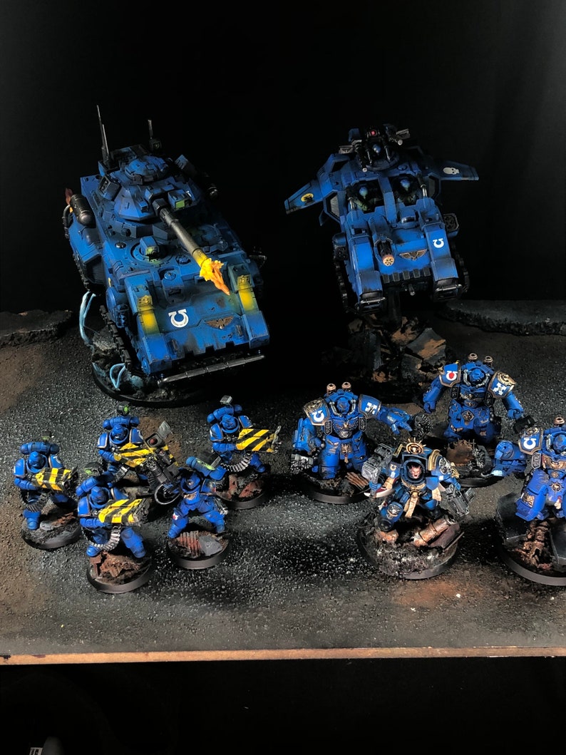 K&ouml;nnte beinhalten: Ein blaues und gelbes bemaltes Miniatur-Krieger-Armeeset mit zwei Fahrzeugen, einem Panzer und einem Flugobjekt sowie einer Soldatenstaffel.