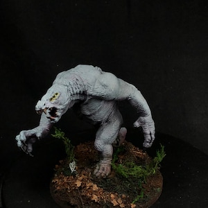 May include: A hand-painted miniature of a grey, monstrous creature with multiple eyes, standing on a base covered in brown dirt and green moss.