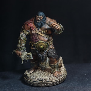 May include: A detailed figurine of a muscular, angry giant with a dark beard, holding a small animal. The giant wears armor and a shield, with a pipe in his mouth. The figure is painted in shades of brown, red, and gold, standing on a textured base.