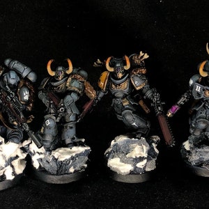 May include: Four grey and black painted miniature figures of space marines with horned helmets, holding weapons and standing on small rocky bases. The figures are painted with details in orange, yellow, and purple.