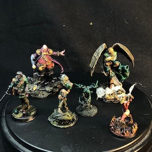 Könnte beinhalten: Eine Sammlung von sechs bemalten Miniaturfiguren auf runden Sockeln. Die Figuren sind in verschiedenen Farben gehalten, darunter Grün, Rot, Blau und Braun. Die Figuren sind in verschiedenen Action-Posen dargestellt.