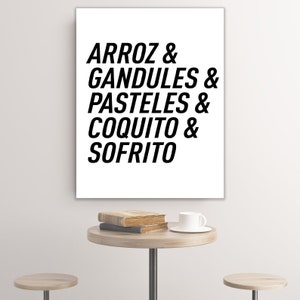 Może przedstawiać: Biały wydruk na płótnie z czarnym tekstem, który brzmi "ARROZ & GANDULES & PASTELES & COQUITO & SOFRITO". Wydruk wisi na białej ścianie nad drewnianym stołem z książkami i białą filiżanką do kawy.