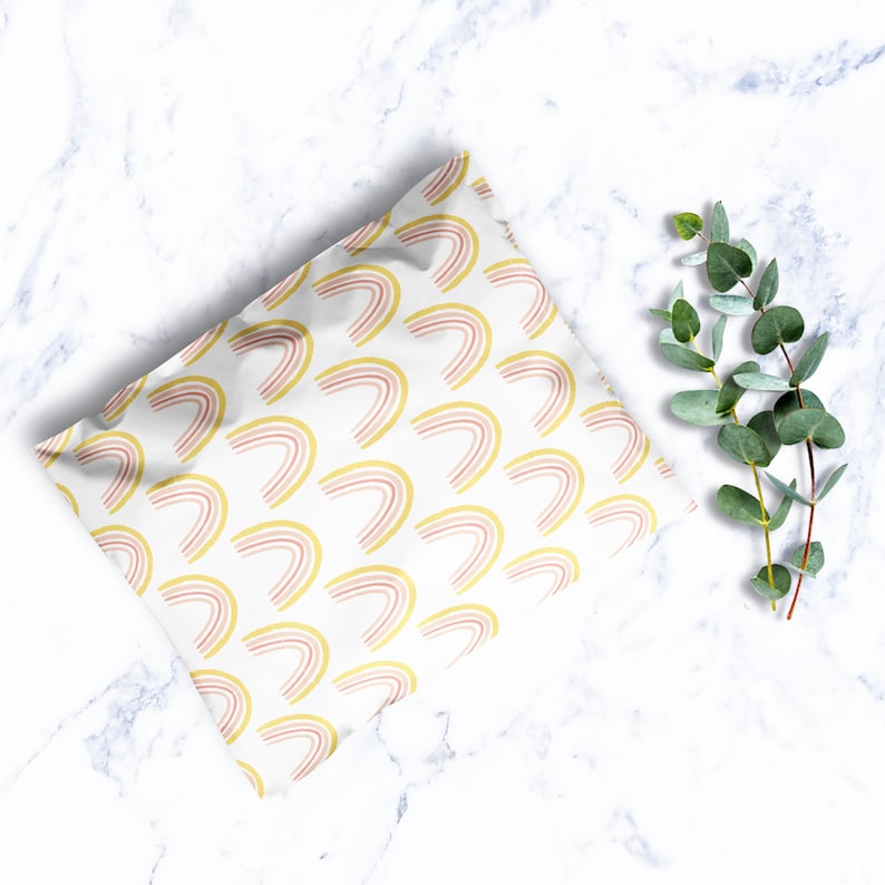 May include: White poly mailer with a repeating pattern of pink and yellow rainbows. The mailer is lying flat on a white marble surface.
