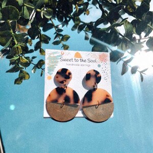 May include: A pair of handmade earrings with a tortoiseshell pattern and gold accents. The earrings are on a white card with the text "Sweet to the Soul Handmade Earrings".