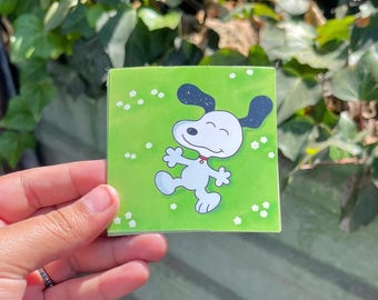 Peut inclure: Un autocollant vert avec un chien de dessin animé blanc aux oreilles noires et un collier rouge. Le chien sourit et a les yeux fermés. L'arrière-plan est vert avec des points blancs.
