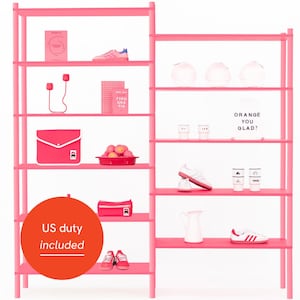 May include: A pink shelving unit with various items on display: a book, shoes, a clutch, a pencil case, and a bowl of oranges. The text "ORANGE YOU GLAD?" is visible. A red circle with the text "US duty included" is also present.
