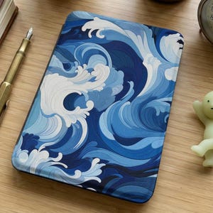 Puede incluir: Una taza de cerámica blanca con asa negra y el texto "But First, Coffee" en negrita negra. La taza se encuentra sobre un fondo borroso, sugiriendo un ambiente acogedor.