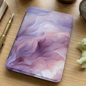 Puede incluir: Una funda rectangular para tableta con un diseño fluido en tonos morado, rosa y blanco. La funda tiene un acabado liso y un borde oscuro. El diseño se asemeja a nubes de acuarela o abstractas.